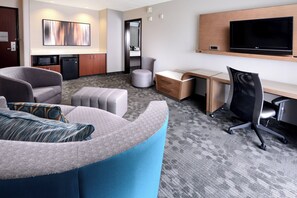 A hotel room with a sofa, a desk, a chair, a television, and a microwave. - Courtyard by Marriott Houston Northwest (Houston)