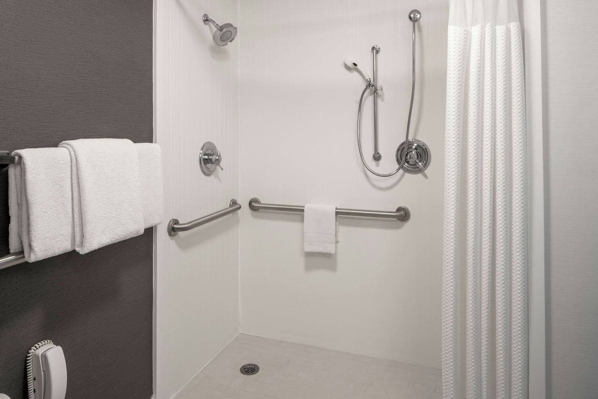 A walk-in shower with a grab bar, a towel rack, and a showerhead.