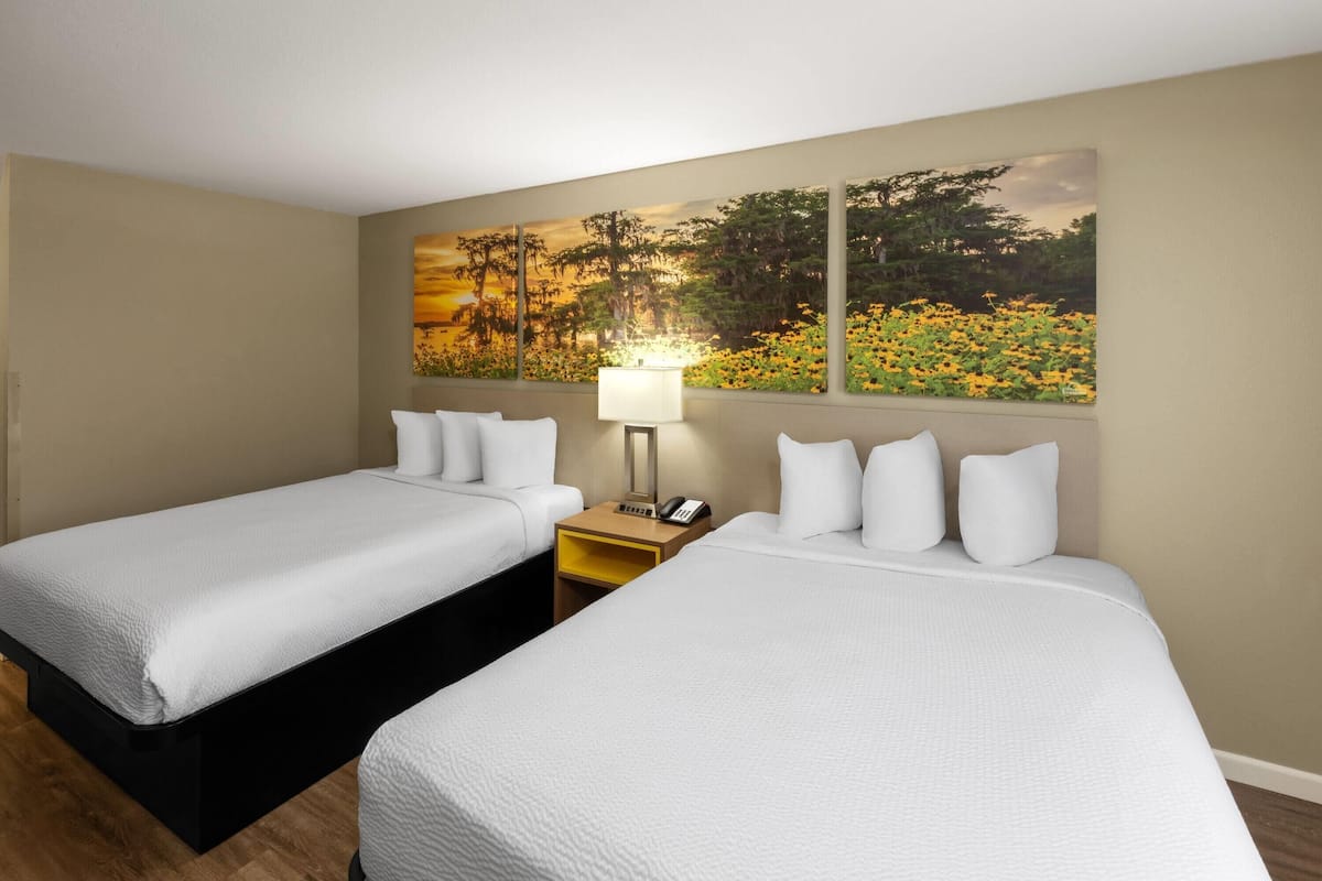 A hotel room with two beds, a nightstand with a lamp, and a large painting on the wall.
