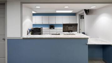 A modern kitchen with white cabinets, a blue accent wall, and a marble countertop.