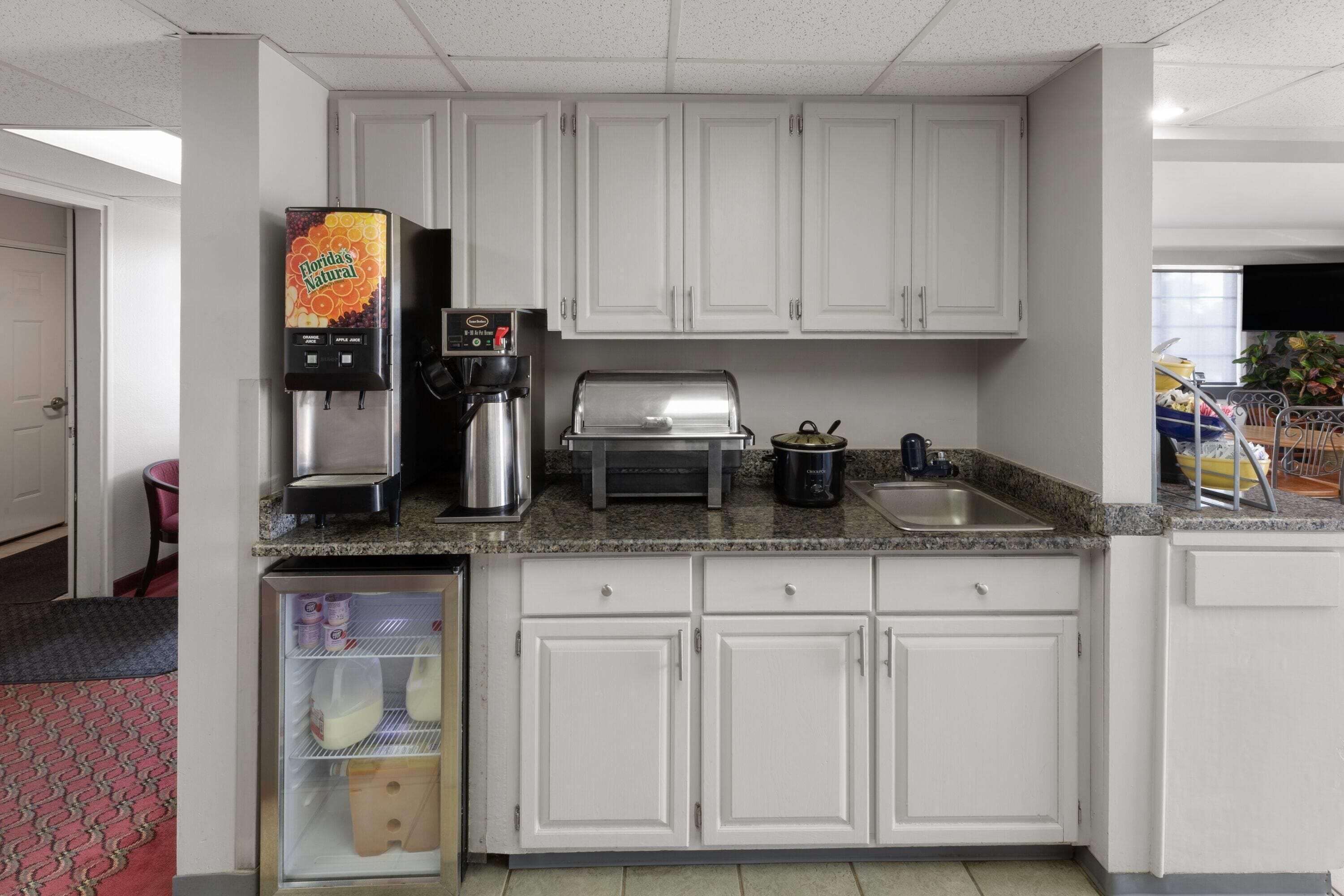 A kitchen with white cabinets, a coffee machine, a grill, and a refrigerator.