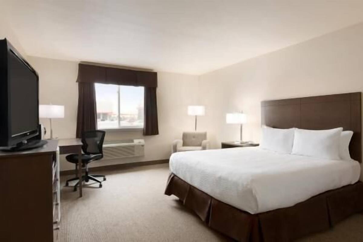 Ein Hotelzimmer mit Bett, Schreibtisch mit Fernseher, Stuhl, zwei Nachttischlampen und einem Fenster mit Vorhängen.