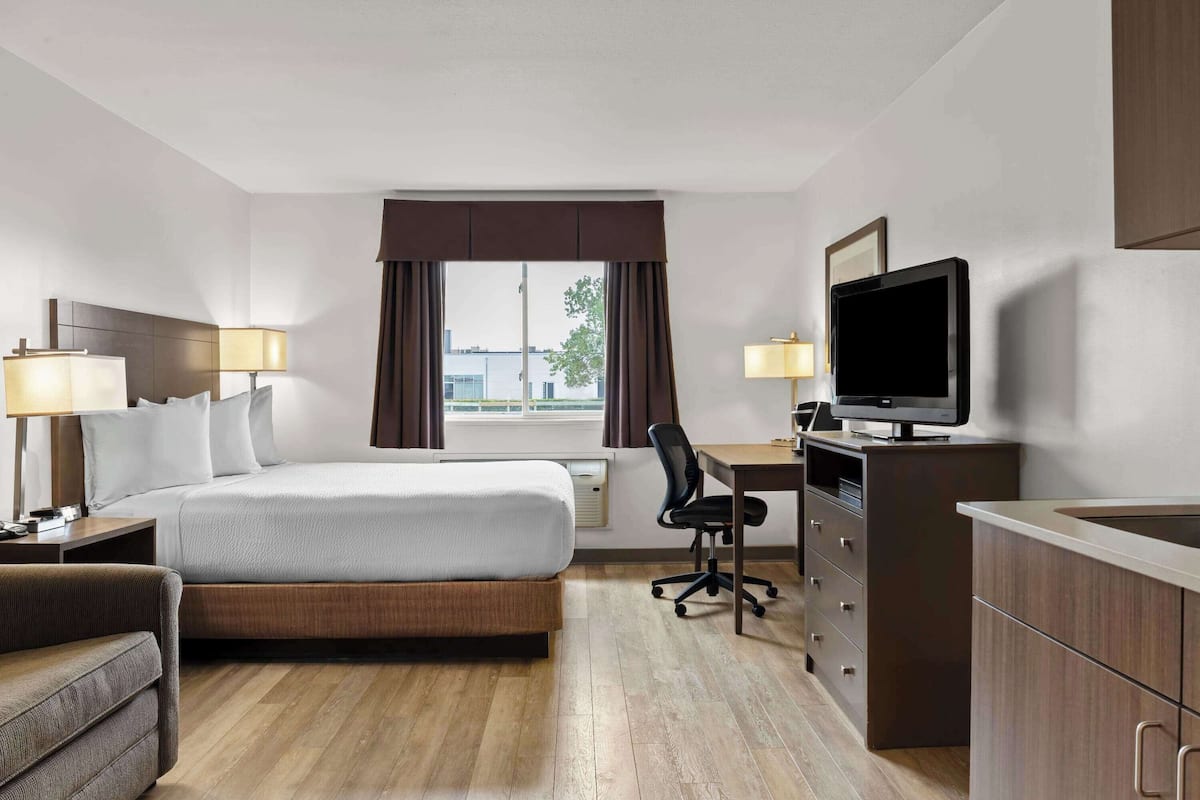 Ein Hotelzimmer mit Bett, Schreibtisch, Sessel, Fernseher und Blick auf die Stadt.