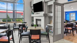 Un espace repas moderne, doté de tables et de chaises, d’une cheminée et d’une grande fenêtre donnant sur l’extérieur.