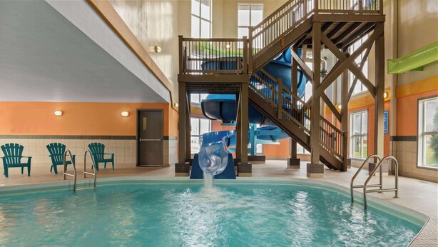 Une piscine intérieure avec un toboggan, de nombreux fauteuils et un escalier menant à une terrasse supérieure.