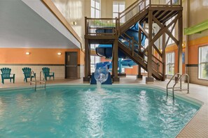 An indoor swimming pool with a water slide, multiple chairs, and a staircase leading to an upper deck. - Days Inn by Wyndham Steinbach (Steinbach)