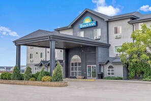 A Days Inn hotel with a covered entrance, a large planter, and a well-maintained garden. - Days Inn by Wyndham Steinbach (Steinbach)