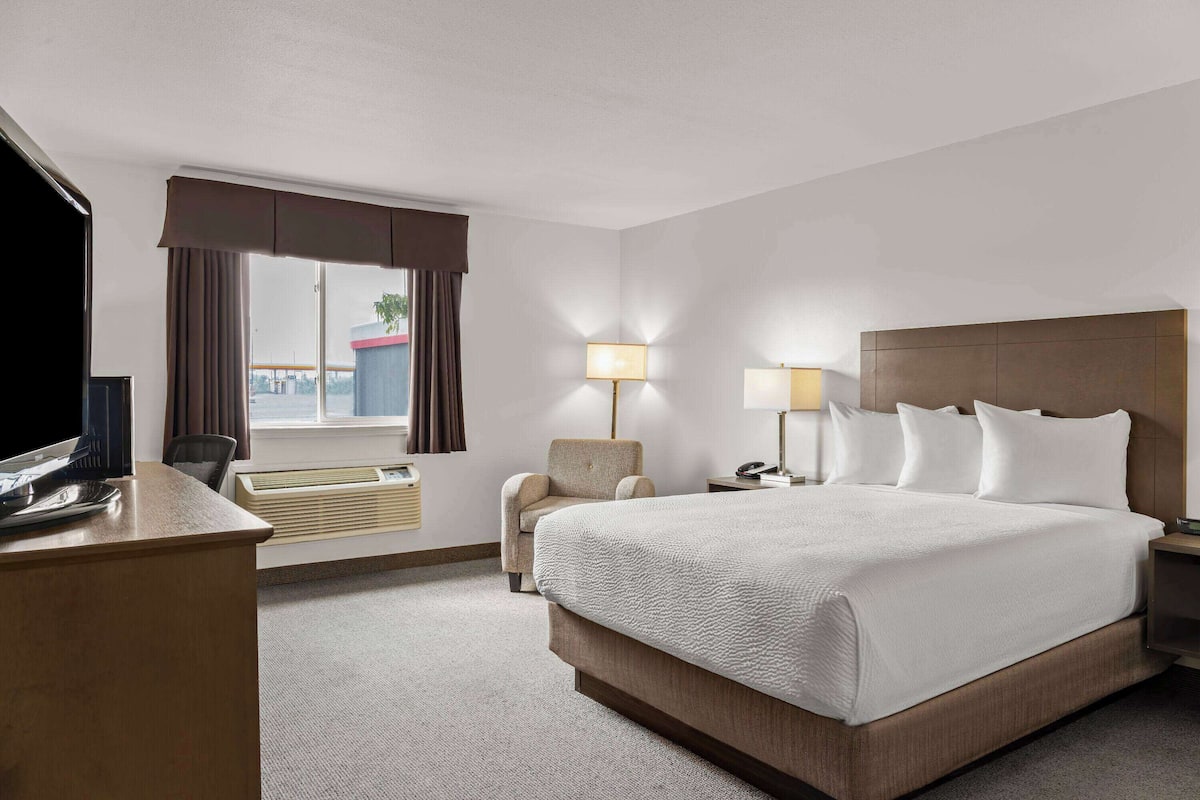 Ein Hotelzimmer mit einem großen Bett, einem Schreibtisch, einem Stuhl, einem Fernseher und einem fenster mit Vorhängen.