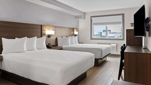 Une chambre d’hôtel avec deux lits, un bureau, une télévision et une grande fenêtre donnant sur la ville.