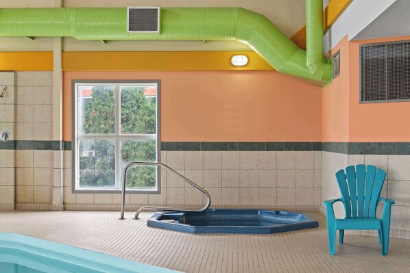 A spa room with a hot tub, a window with a view of greenery, and a blue chair. - Days Inn by Wyndham Steinbach (Steinbach)