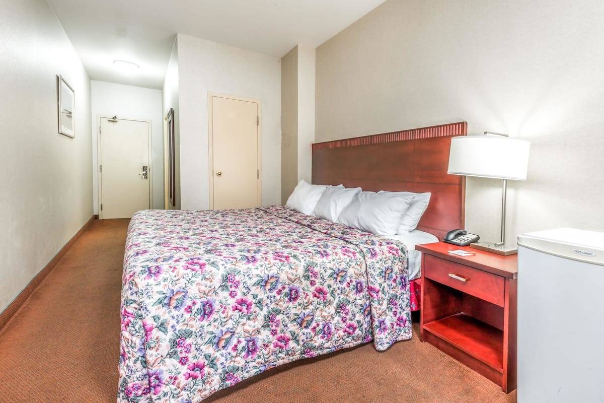 Una habitación de hotel con cama, mesita de noche, lámpara y teléfono.