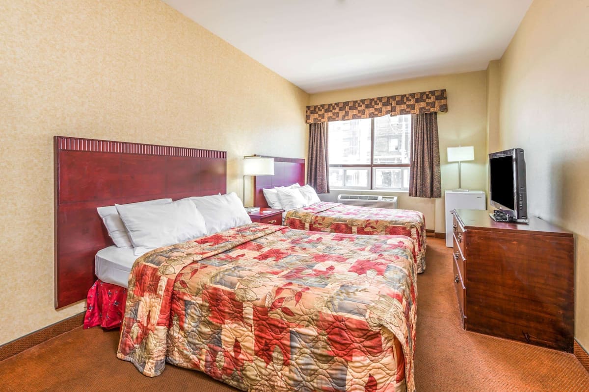 Habitación de hotel con dos camas, televisión, escritorio y ventana con cortinas.