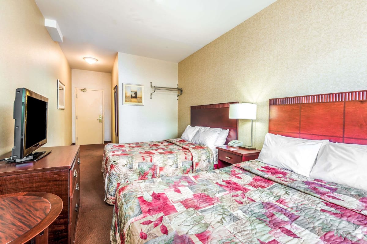 Habitación de hotel con dos camas, un escritorio, un televisor y una puerta.