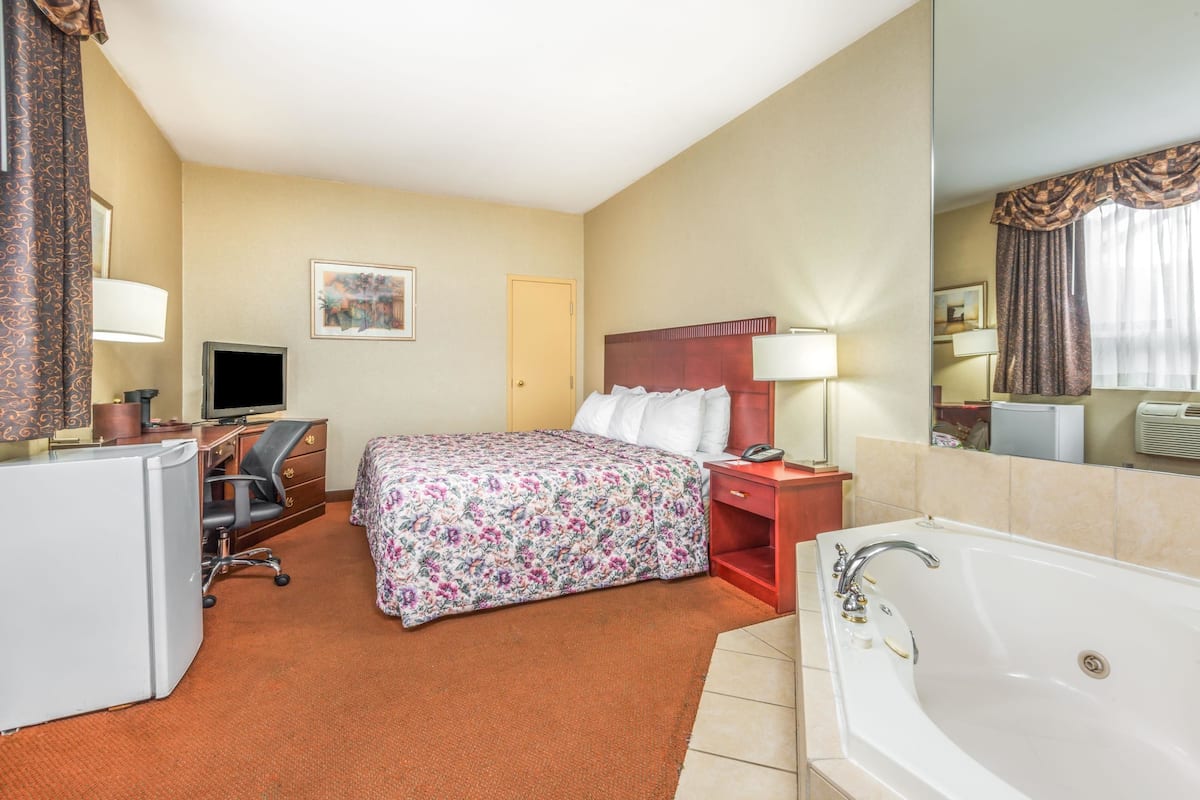 Habitación de hotel con cama, escritorio, silla, televisor y un baño amplio con bañera.