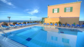 Una piscina al aire libre, sombrillas, sillones reclinables de piscina