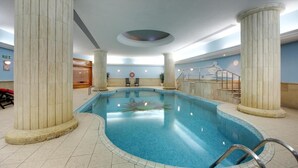 An indoor swimming pool with marble columns, a lifebuoy, and a staircase leading to a balcony.