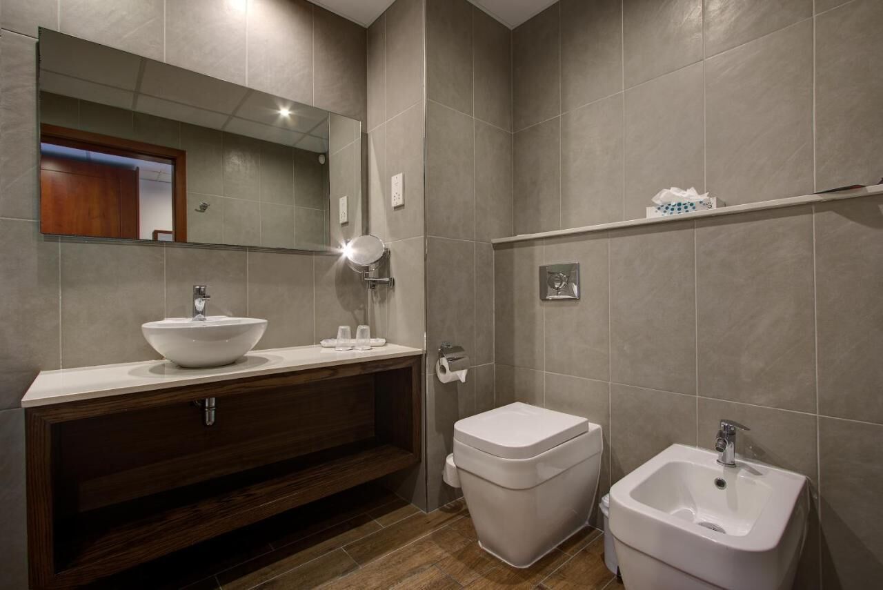 Une salle de bain moderne avec un grand miroir, un lavabo sur colonne, des toilettes et un bidet.