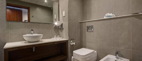 Une salle de bain moderne avec un grand miroir, un lavabo sur colonne, des toilettes et un bidet.