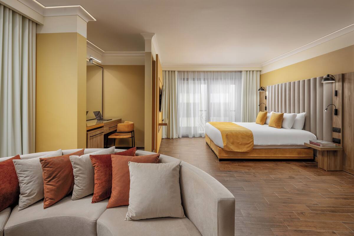 A hotel room with a sofa, a bed, a desk, and a mirror.