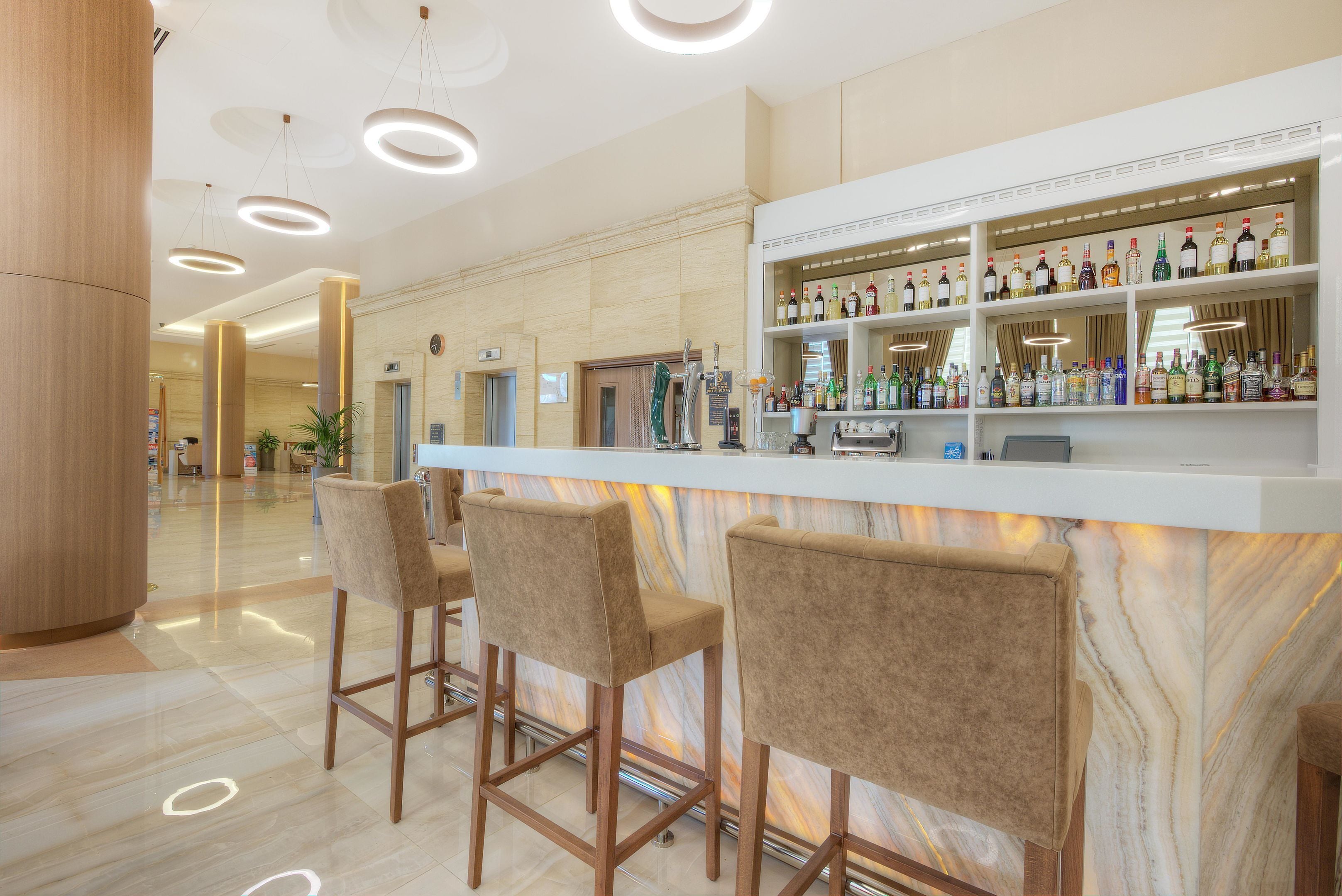 A bar area with a marble countertop, bar stools, and a variety of liquor bottles.