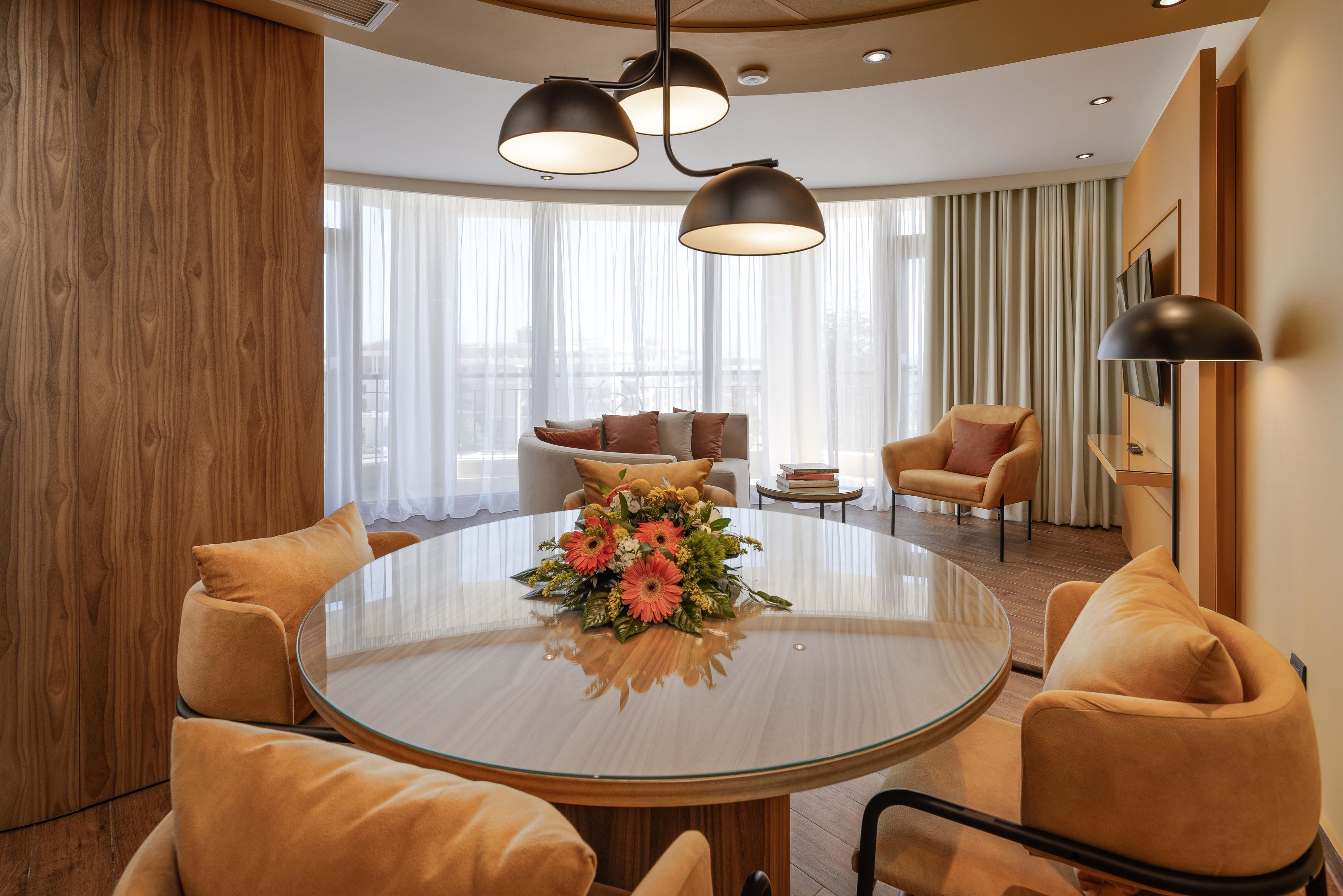 A modern dining area with a round glass table, two black pendant lights, and a floral centerpiece.