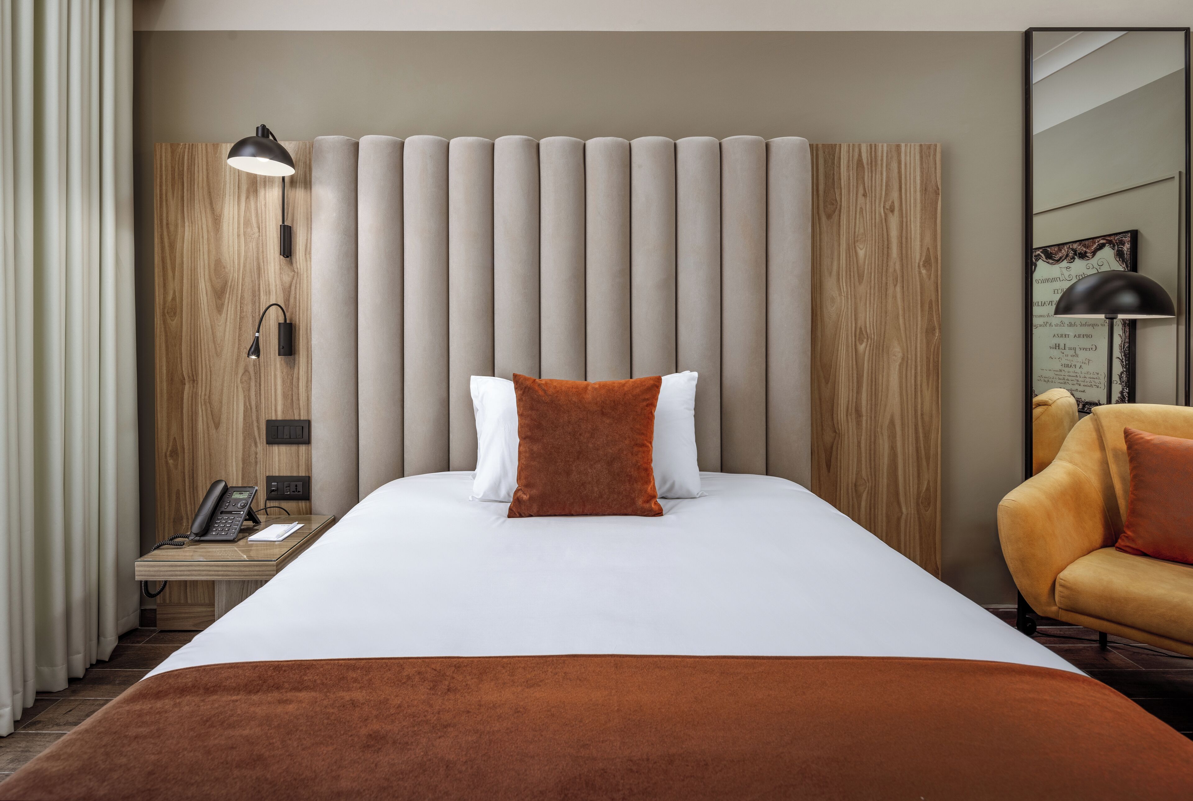 A hotel room with a large bed, a wooden headboard, a bedside table with a phone, and a chair.