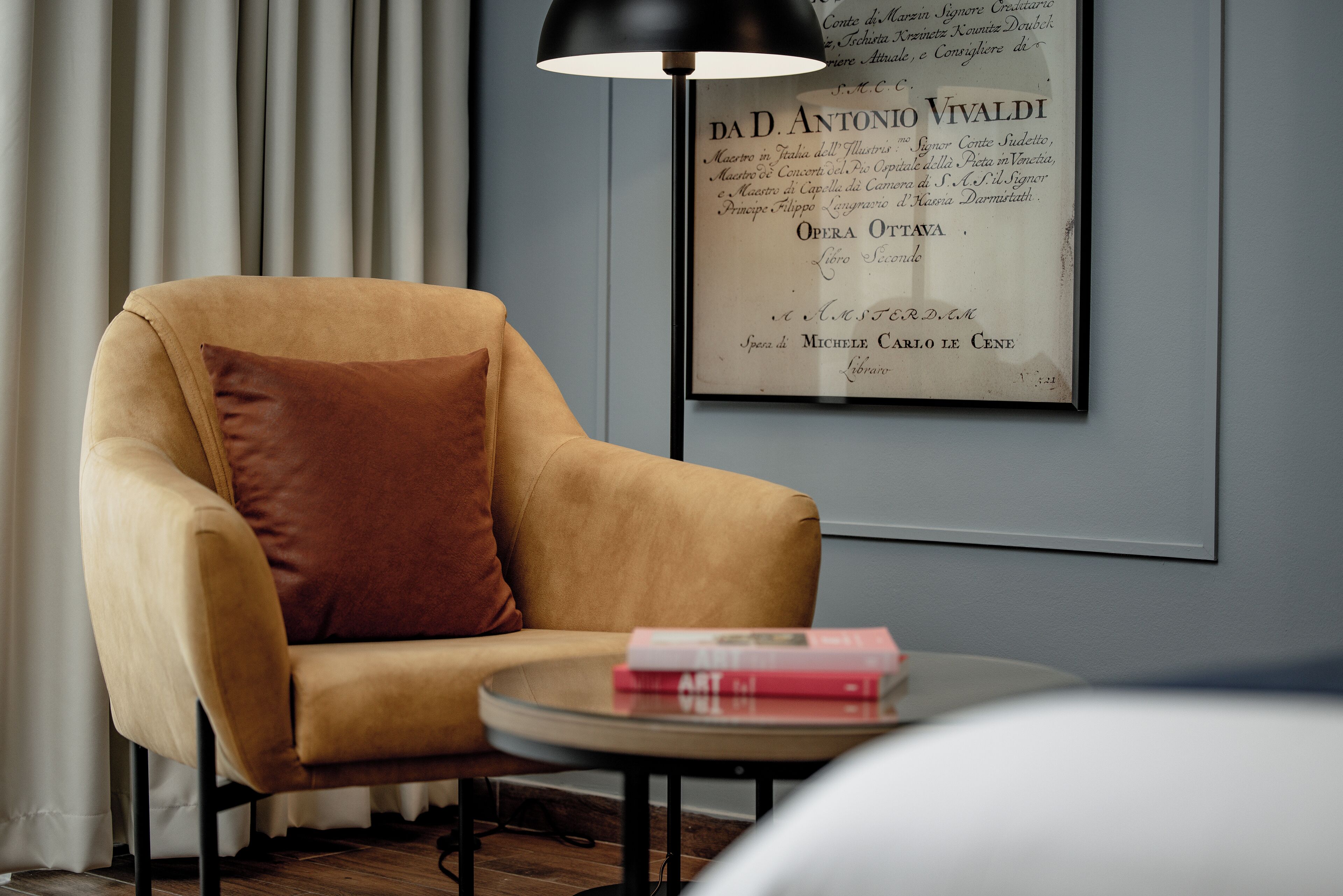 Ein modernes Zimmer mit einem beigefarbenen Sessel, einem runden Tisch mit Büchern und einem gerahmten Zertifikat an der Wand.