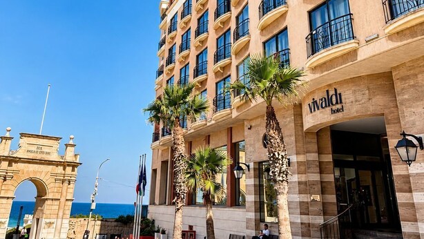 A multi-story hotel with balconies, a stone archway, and palm trees.