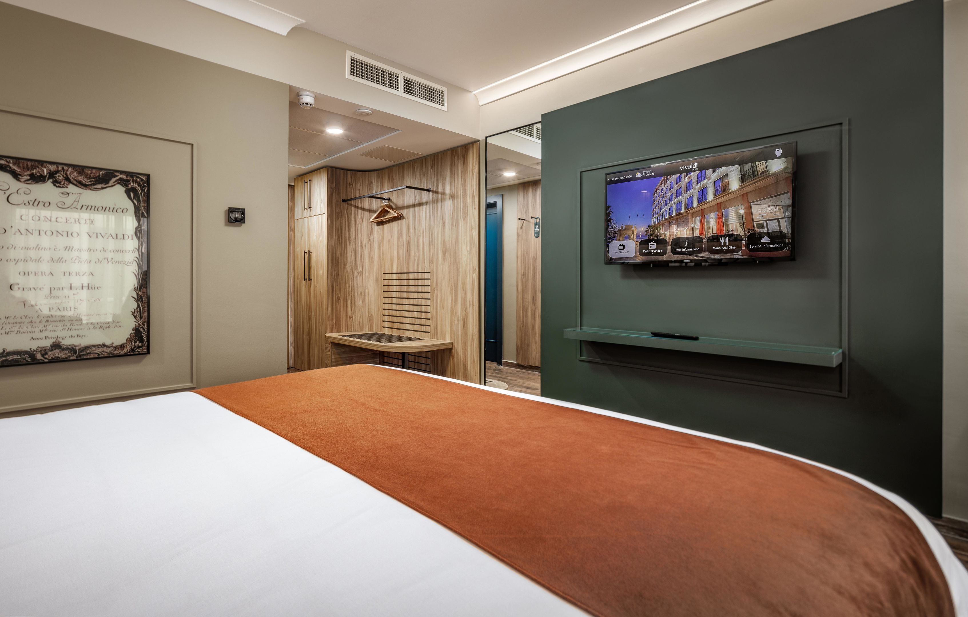 A hotel room with a bed, a television mounted on the wall, and a framed menu on the wall.