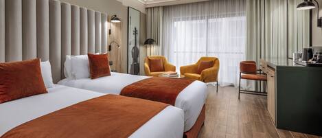 A hotel room with two beds, a desk, a chair, a lamp, and a large window with curtains.