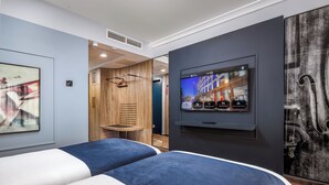 A modern hotel room with two beds, a mounted TV, and a wooden cabinet.