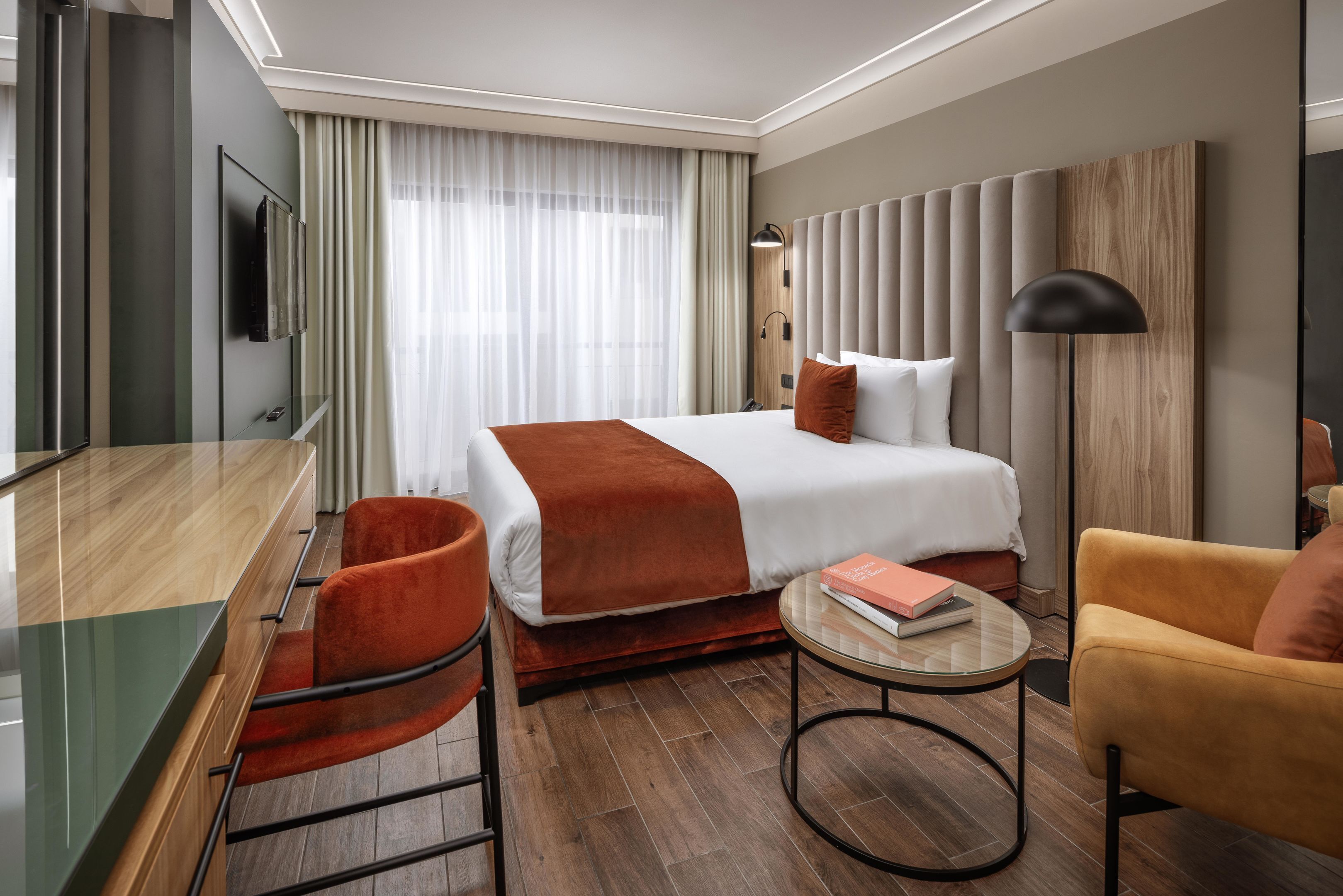 A hotel room with a bed, a desk, a chair, a round table, and a TV.