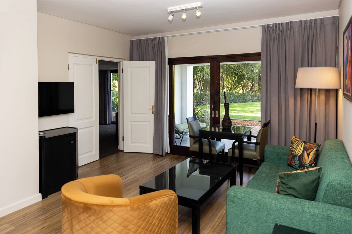 A modern living room with a green sofa, a yellow armchair, a glass coffee table, a flat-screen TV, and a dining area with a table and chairs.
