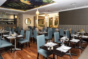 A restaurant with multiple tables set for dining, featuring a modern interior with wooden flooring and blue upholstered chairs. - Lord Charles Hotel (Cape Town)