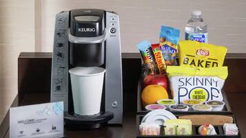 Een koffiezetapparaat, een waterfles, snacks en een welkomstbord op een hotelbalie.