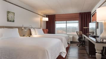 Une chambre d’hôtel avec deux lits, un bureau, une chaise, une lampe, une fenêtre avec des rideaux et une vue sur l’extérieur.