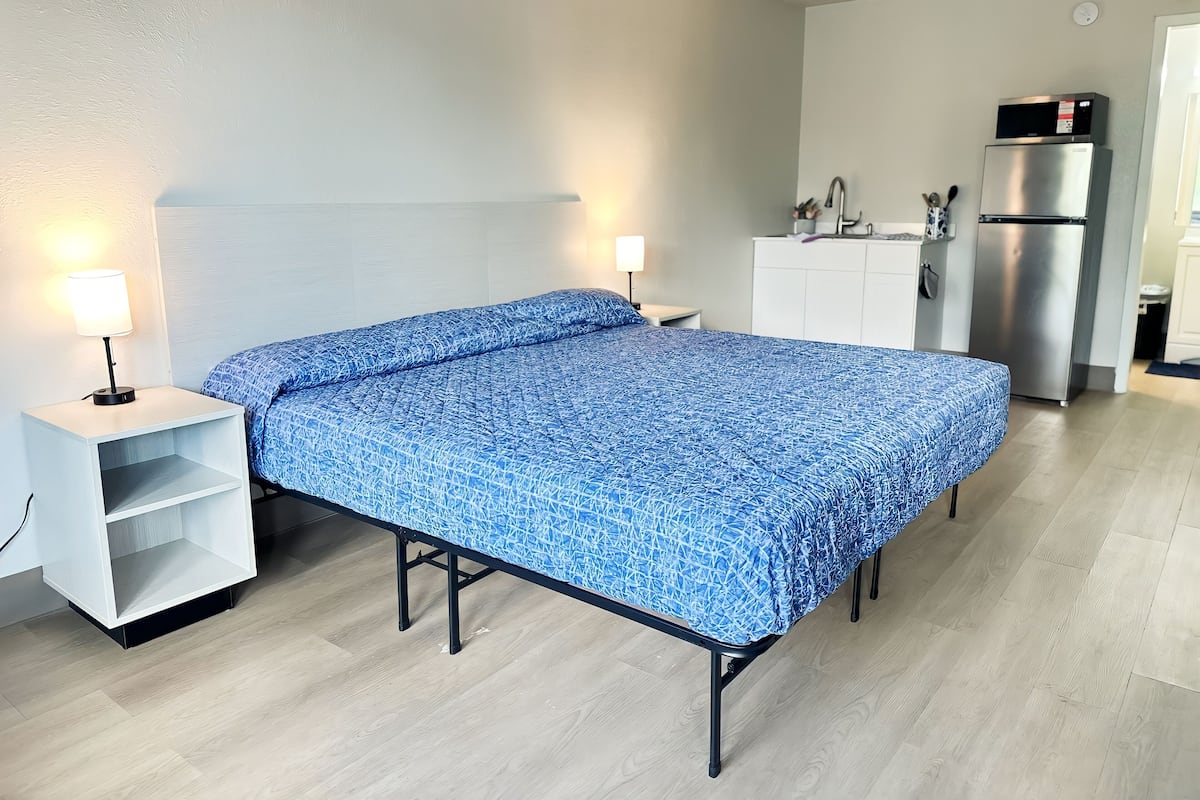 Ein Schlafzimmer mit Bett, Nachttischen, einem Schreibtisch, einem Kühlschrank und einer kleinen Küchenzeile.