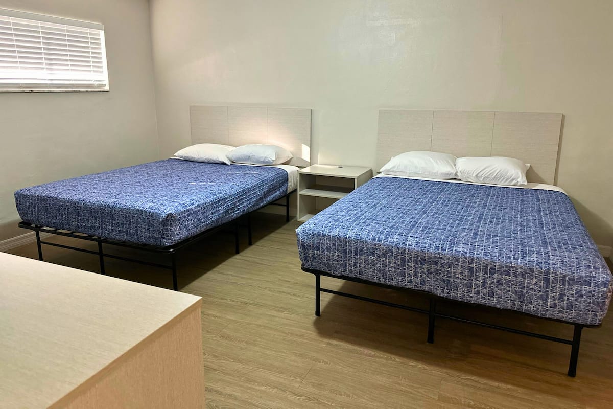 Ein Hotelzimmer mit zwei Einzelbetten, einem Nachttisch mit Lampe und einem Holztisch.
