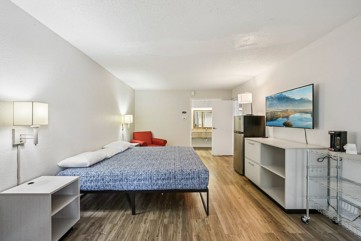 Ein modernes Hotelzimmer mit Bett, Schreibtisch, Stuhl, Fernseher und Küchenzeile.