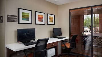 A business center with two computer stations, framed artwork, and a sign indicating 24-hour access.