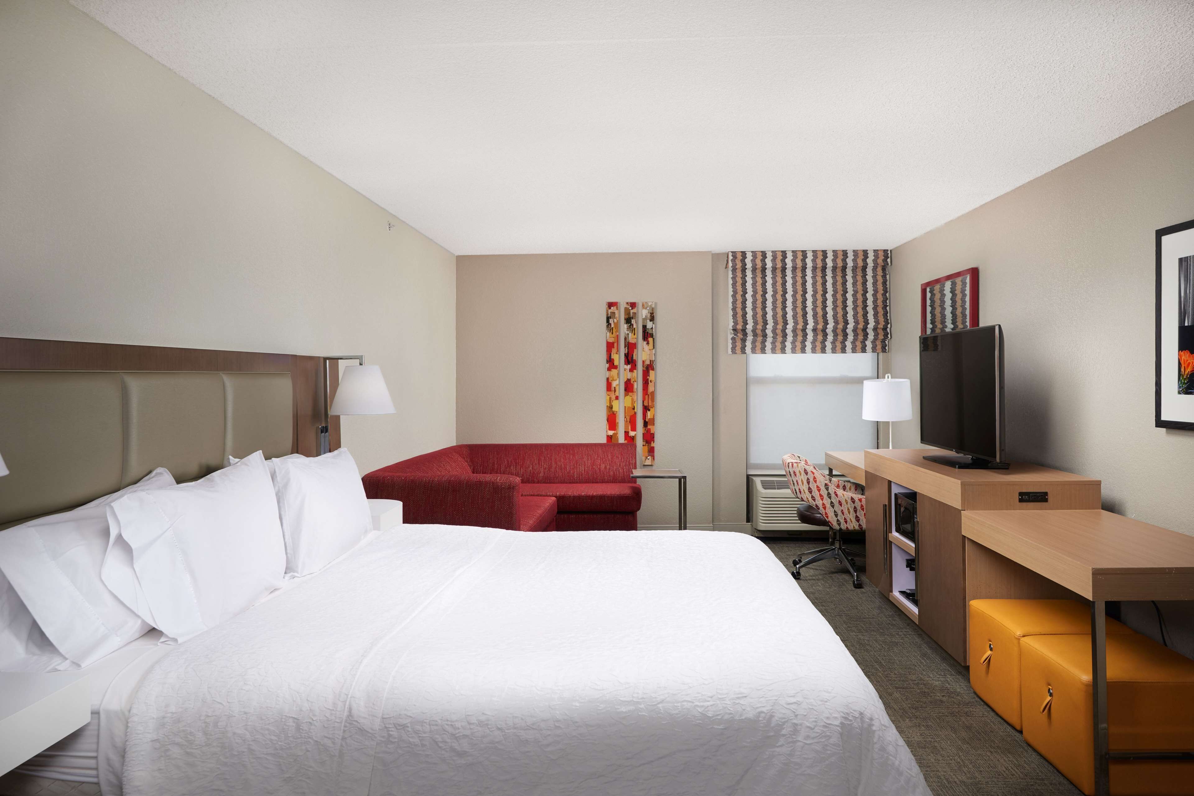 A hotel room with a large bed, a red sofa, a television, and a desk with a computer.