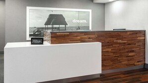 A hotel reception desk with a wooden panel design, a large framed picture of a beach scene, and a sign reading "Hilton Honors".