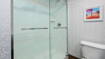 Ein modernes Badezimmer mit Duschkabine aus Glas, einer weißen Toilette und einer Wand mit geometrischem Muster.
