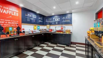 Una cocina con equipo para hacer gofres, piso de cuadros y una pared con texto e ilustraciones sobre gofres.