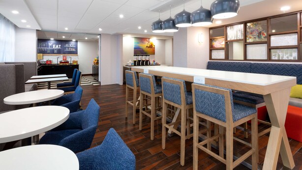 A modern restaurant with a long counter, blue upholstered chairs, and a bar area.