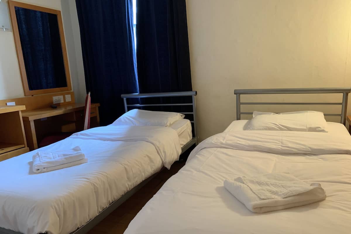 Deux lits simples avec du linge de lit blanc, un bureau en bois et un miroir au mur.