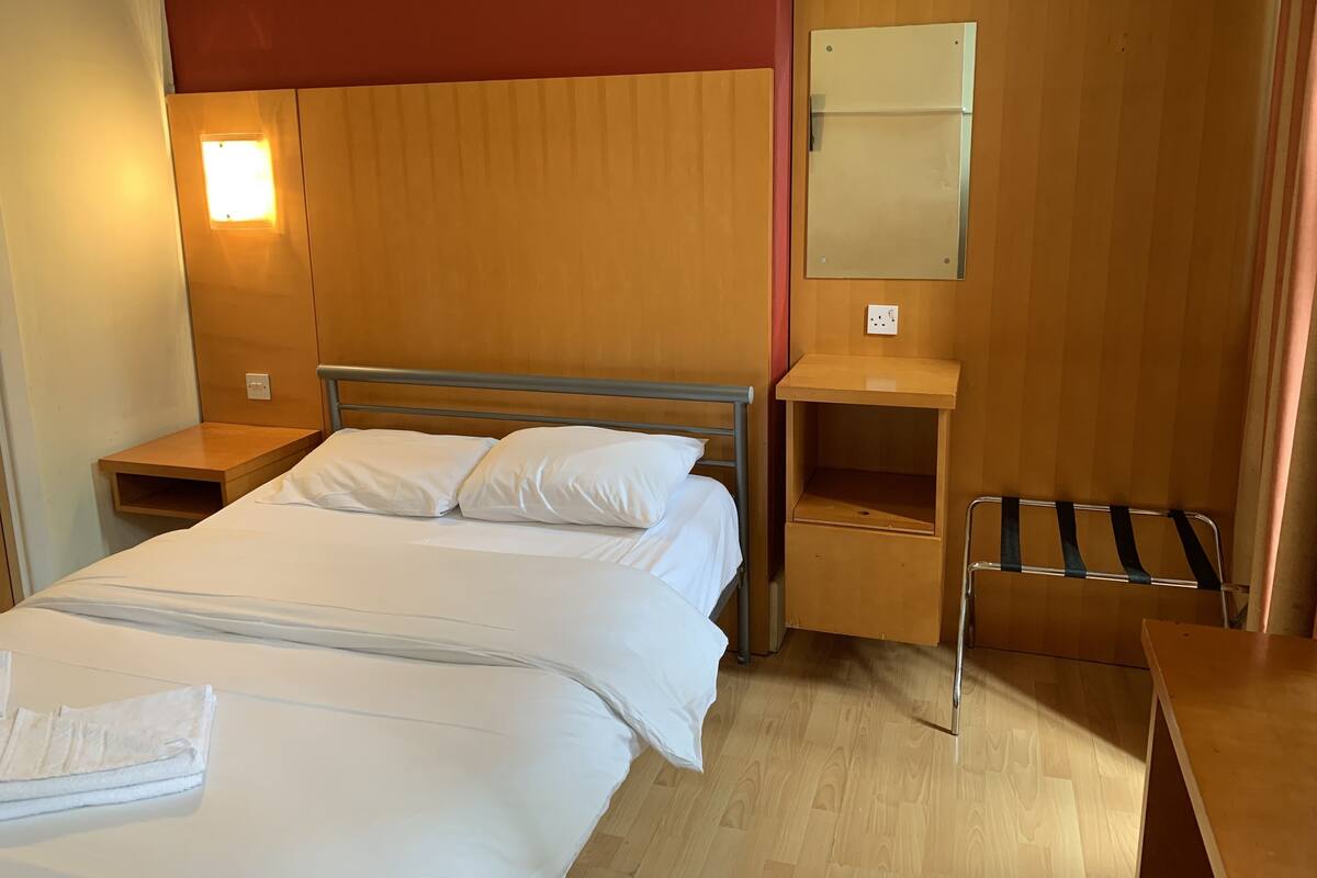 Une chambre d’hôtel avec un lit, une table de chevet, une table de chevet en bois, un miroir et une serviette sur le lit.