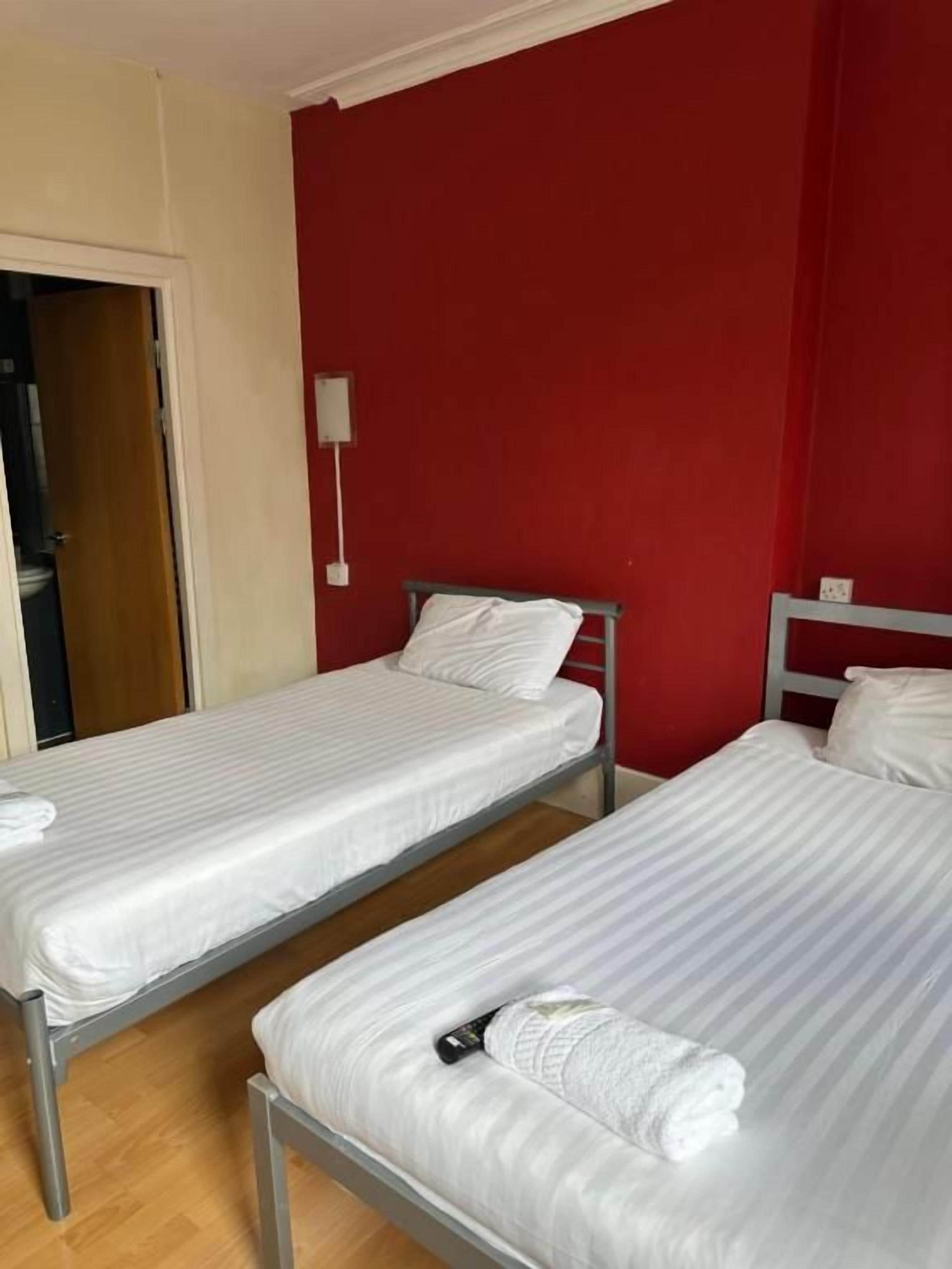 Una habitación con dos camas individuales, una puerta de madera y una pared roja.