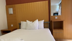 Una cama bien hecha con sábanas y almohadas blancas, un cabecero de madera, una mesita de noche pequeña y un mueble estante empotrado.