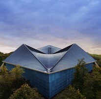 Un edificio moderno de arquitectura con un diseño triangular único, rodeado de un bosque denso.